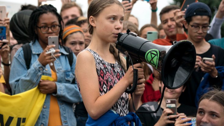 Greta Thunberg with a bullhorn and diverse crowd of young people protesting and taking photos on the phones during the 2018 climate strike